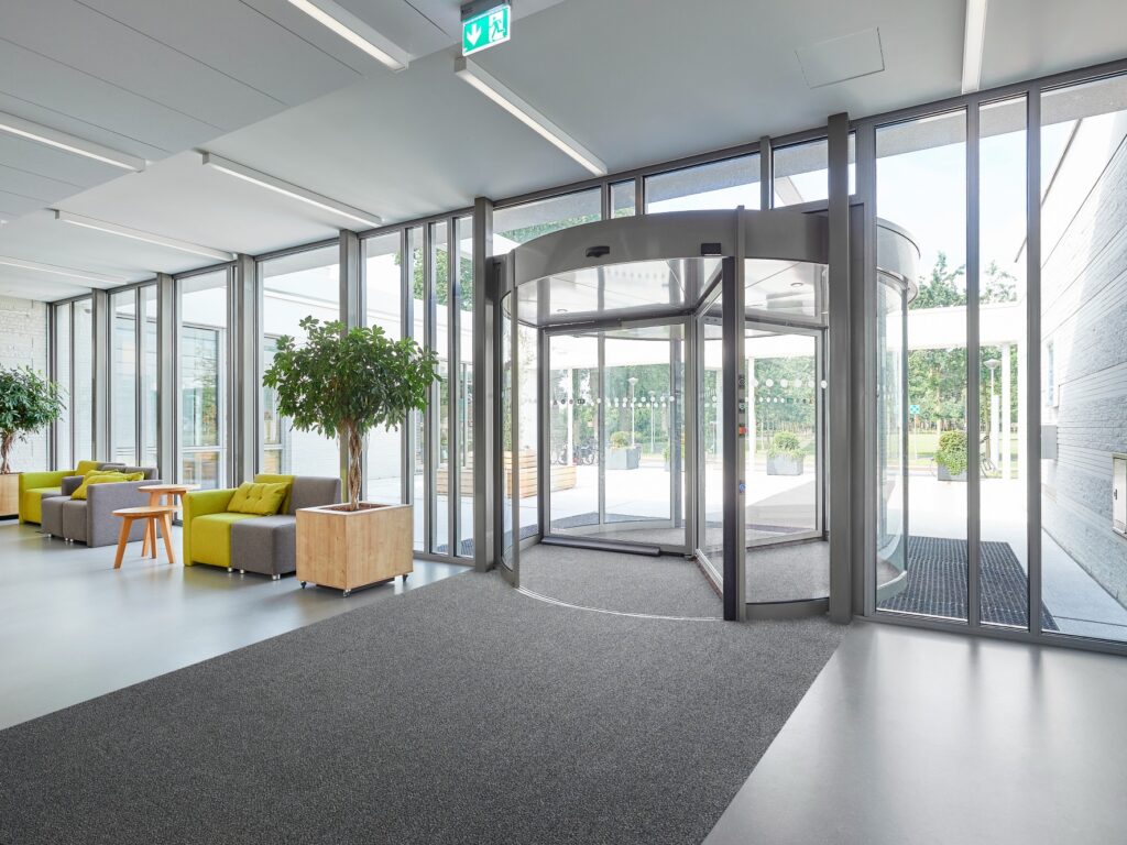 Conversations with Circular Innovators: Rinos on Rethinking Entrance Matting A modern corporate lobby featuring a grey Rinos entrance mat made of ECONYL® regenerated nylon.